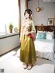 A woman in a yellow kimono standing in front of a bed.