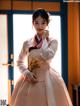 A woman in a pink and white hanbok standing in front of a window.