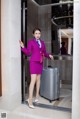 A woman in a purple suit standing next to a suitcase.